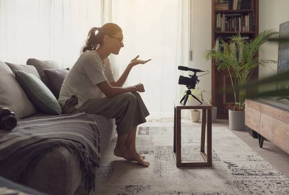 Woman recording video blog at home sitting on couch in cozy living room setting