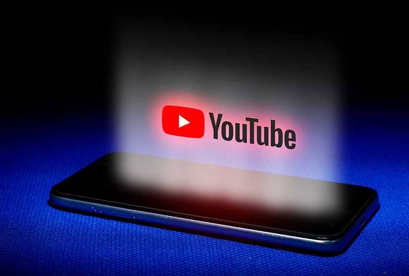 YouTube logo glowing above a smartphone on a blue surface with dark background