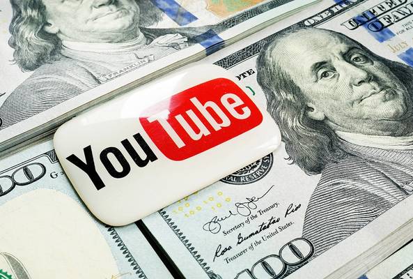 YouTube logo badge placed on top of scattered one hundred dollar bills representing monetization